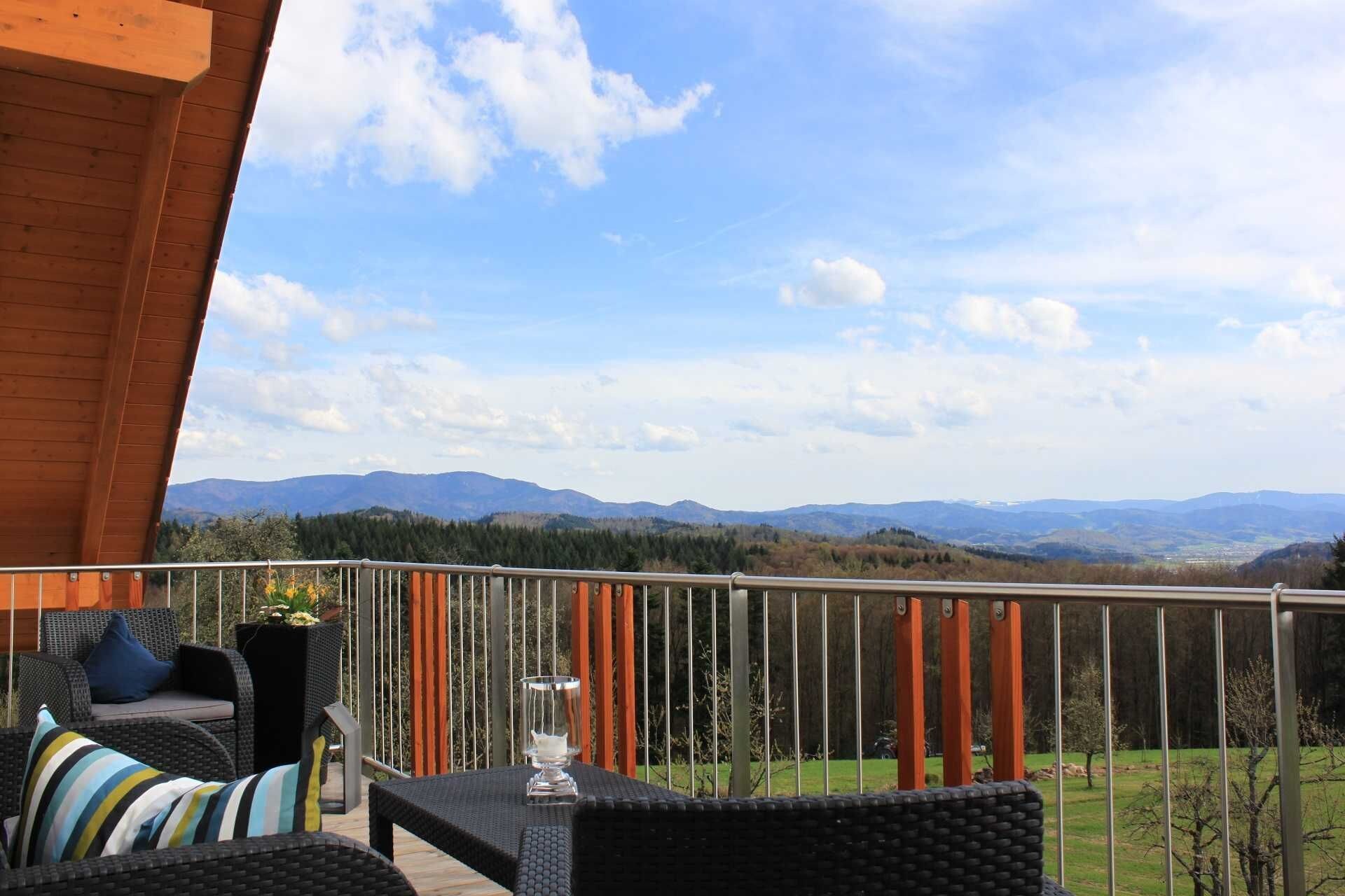 A balcony with wicker furniture, a glass table, and a view of distant mountains.