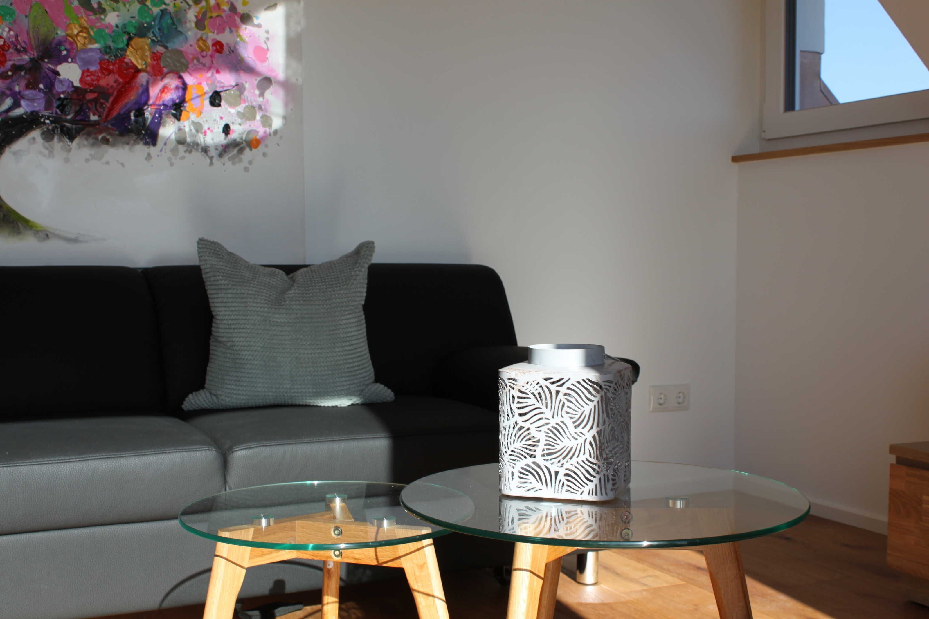 A modern living room with a glass coffee table, a grey sofa, and a decorative vase.