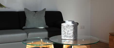 A modern living room with a glass coffee table, a grey sofa, and a decorative vase.