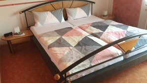 A bed with a metal frame, two pillows, a quilt, a nightstand with a lamp, and a wooden ceiling.