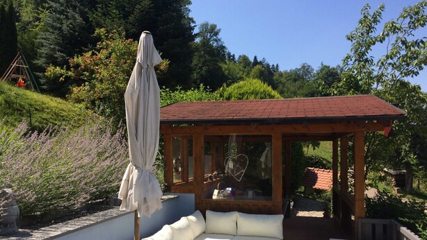 A covered outdoor seating area with a wooden gazebo, cushioned sofas, and a table.