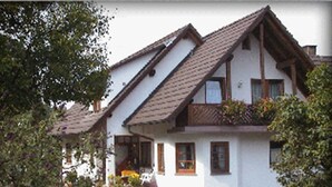 A traditional chalet-style house with a steeply pitched roof, wooden beams, and a balcony with potted plants.
