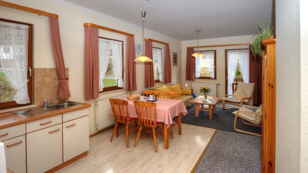 Una cocina compacta con lavamanos y armarios de madera, una zona de comedor con mesa y sillas, y una acogedora sala de estar con sofá y sillones.