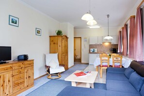 A modern living room with a sofa, a TV, a wooden cabinet, and a dining area with chairs and a table.