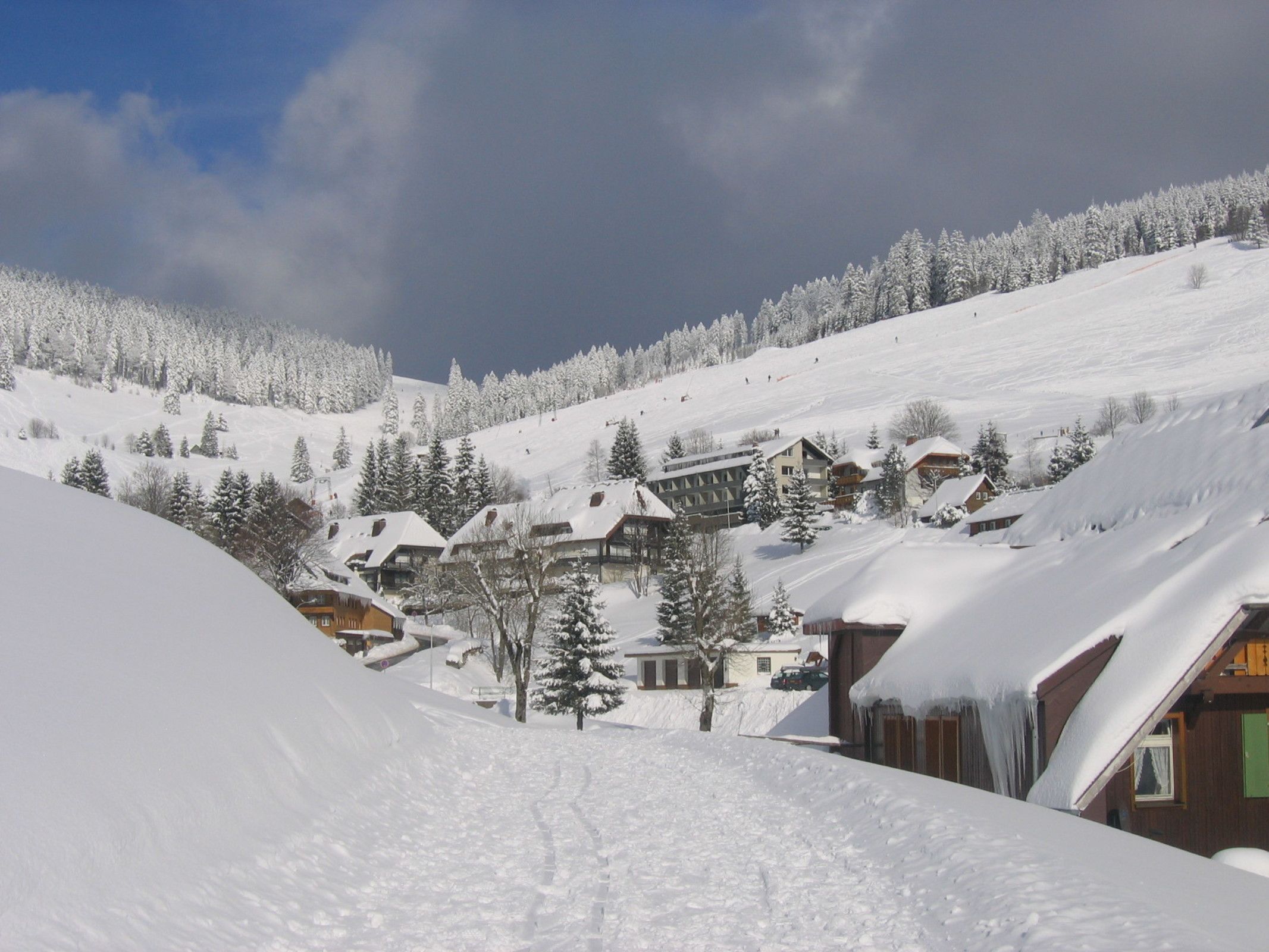 Een besneeuwde dorp met chalets, een skipiste op de achtergrond en een heldere lucht.