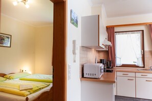 Ein kleines Hotelzimmer mit Bett, Kochnische, einem Fenster mit Vorhängen und einem kleinen Badezimmer.