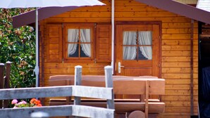 Una cabaña de madera con un porche, dos ventanas con cortinas y un banco.
