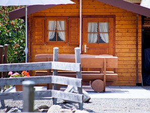 A wooden cabin with a porch, two windows with curtains, and a bench. - Vacation apartment 2 "Stübenbach" - Haus Keller vacation apartments (Todtnau)