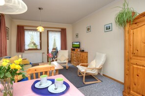 A cozy room with a dining table, chairs, a television, and a wooden cabinet.