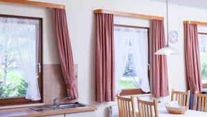 Una cocina con un lavabo, armarios de madera, una mesa de comedor con sillas y una ventana con cortinas.