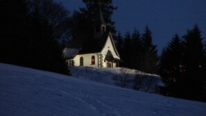 Una pequeña iglesia con campanario, rodeada de árboles y nieve.