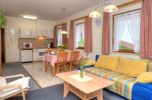 A cozy, well-lit room with a dining table, chairs, a sofa, and a small kitchen area.