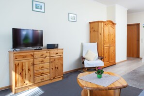 Ein Zimmer mit einem Holzkasten, einem Fernseher, einem Sessel und einem kleinen Tisch mit einer Pflanze.