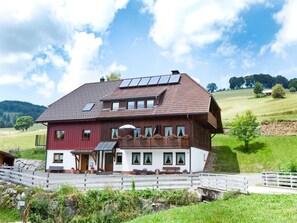 A two-story wooden house with a sloped roof, solar panels, and a balcony with flower boxes.