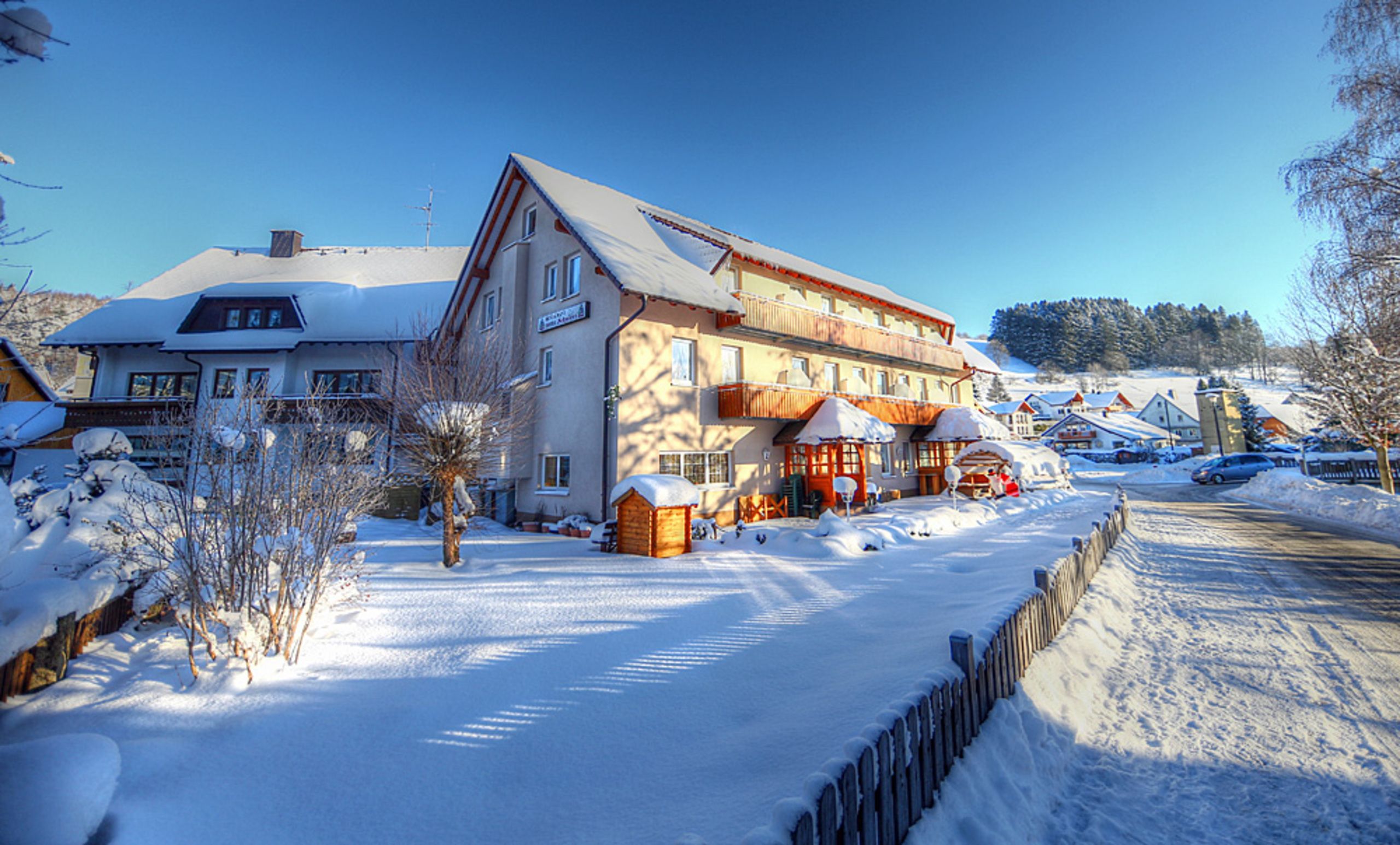 A snow-covered residential area with houses, a wooden fence, and a clear sky.