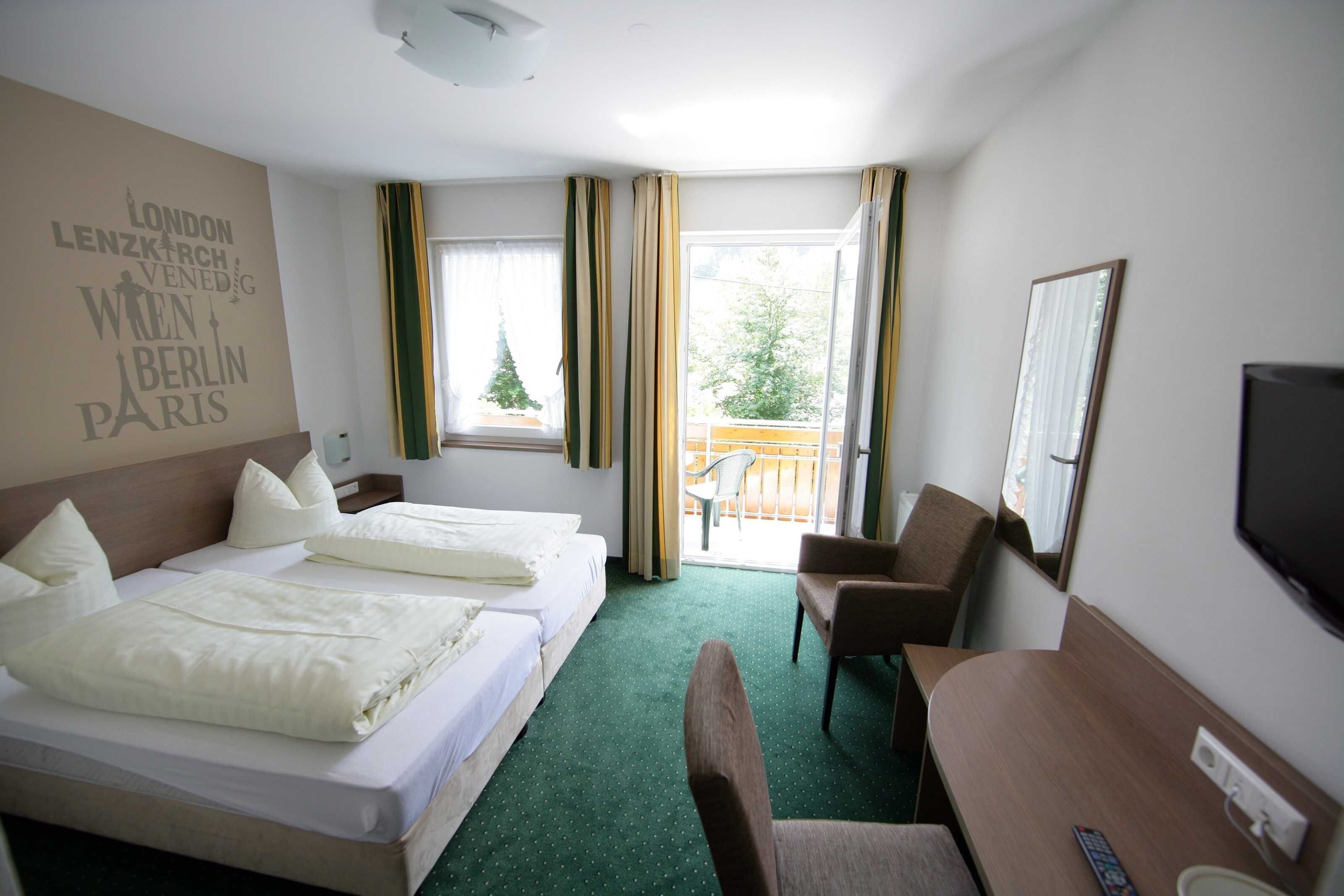 Une chambre d’hôtel avec deux lits, un bureau, une chaise, une télévision et un balcon donnant sur la verdure.