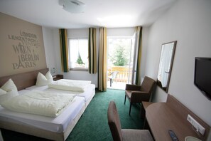 Habitación de hotel con dos camas, un escritorio, una silla, un televisor y un balcón con vistas a árboles.