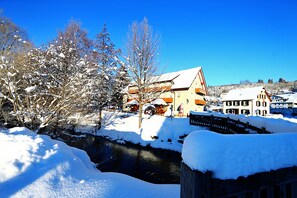 Un pueblo cubierto de nieve con edificios, un río y árboles desnudos.