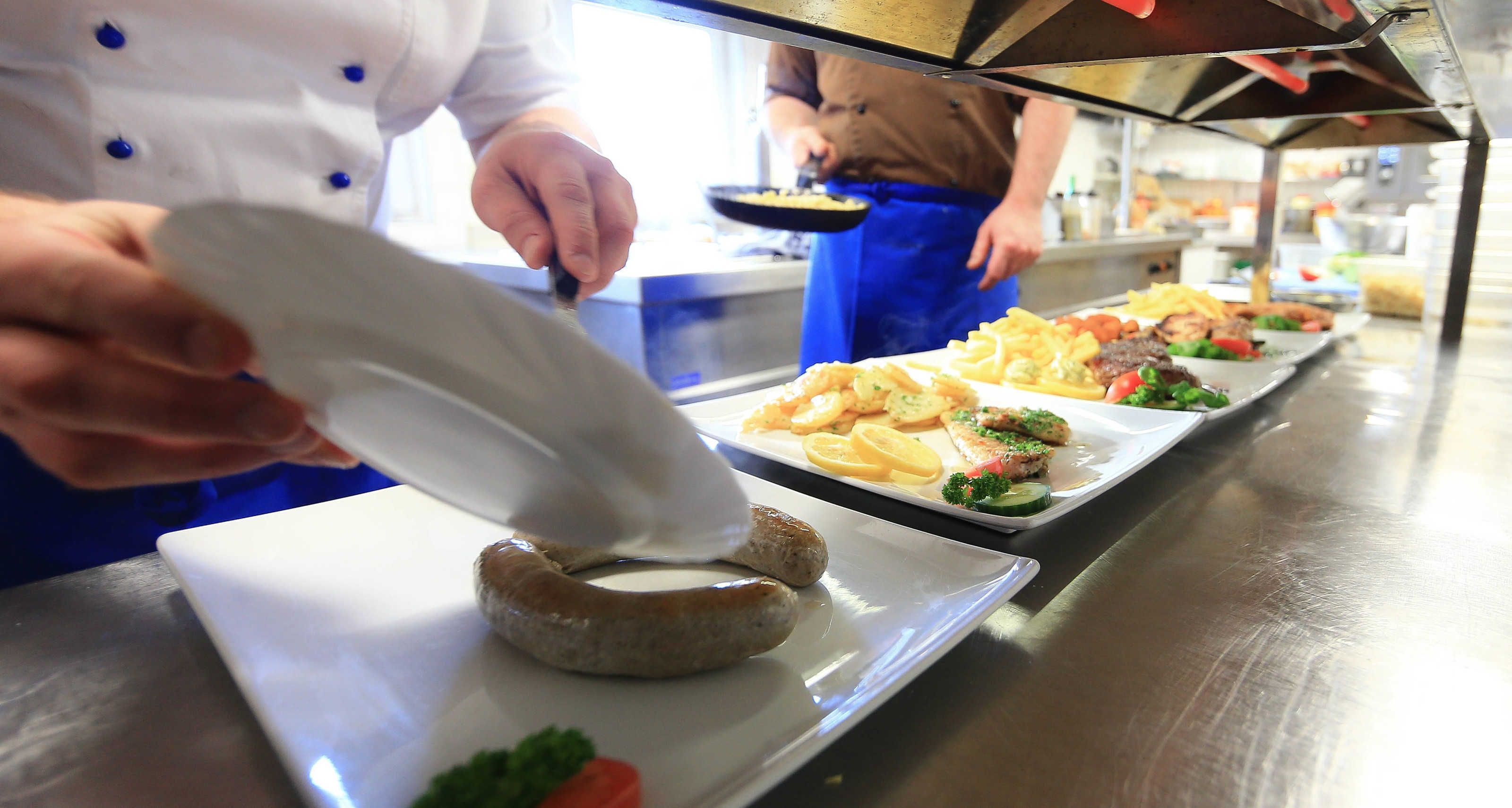 A chef preparing food in a kitchen with stainless steel surfaces and a long counter.