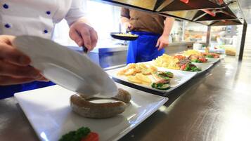 A chef preparing food in a kitchen with stainless steel surfaces and a long counter.