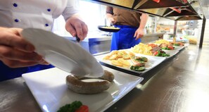 Un chef prepara alimentos en una cocina con superficies de acero inoxidable y una barra larga.