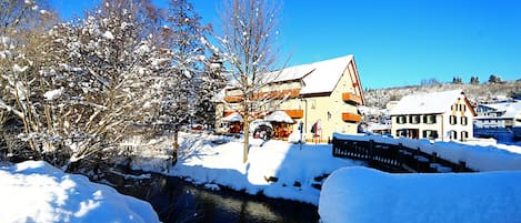 Un pueblo cubierto de nieve con edificios, un río y árboles desnudos.