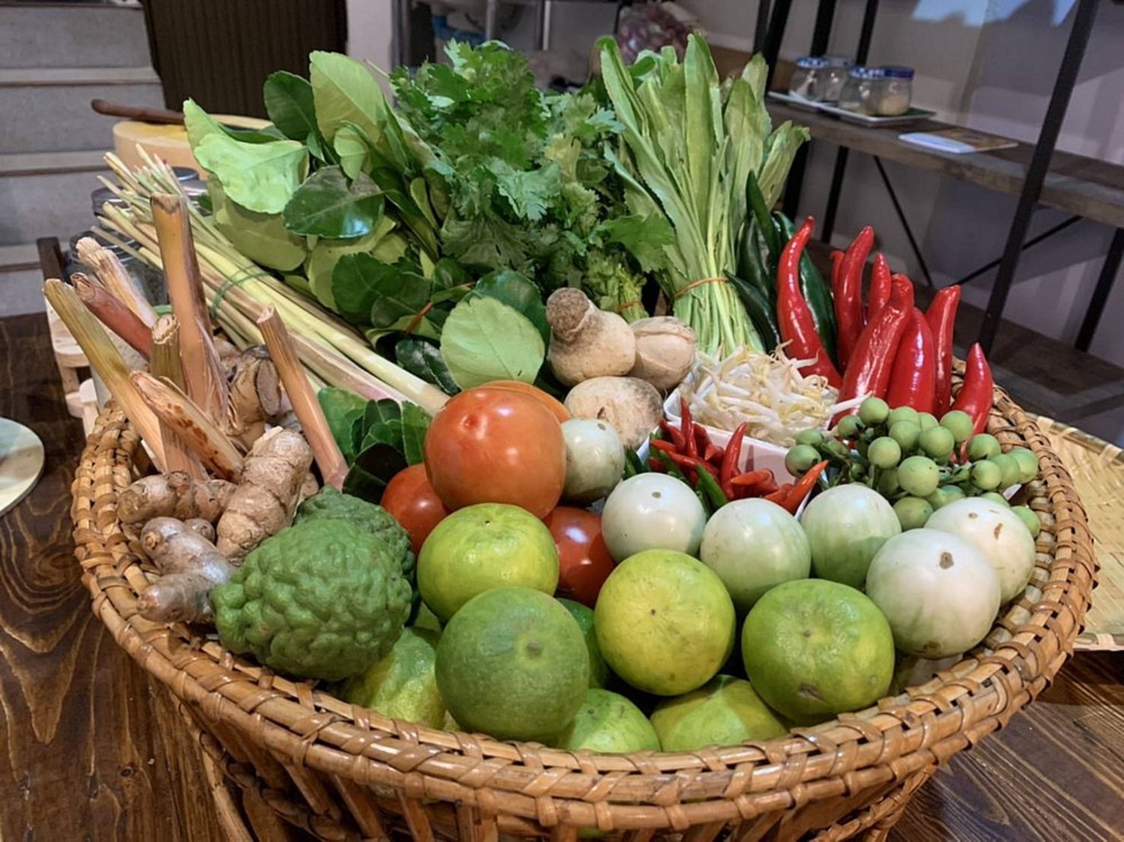 A basket filled with various fresh vegetables and fruits, including tomatoes, limes, and chili peppers.