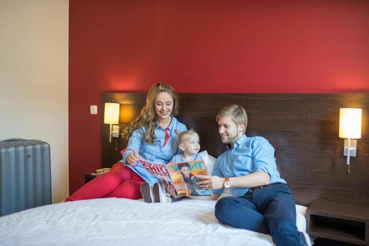 A hotel room with a red accent wall, a wooden headboard, and two bedside lamps.