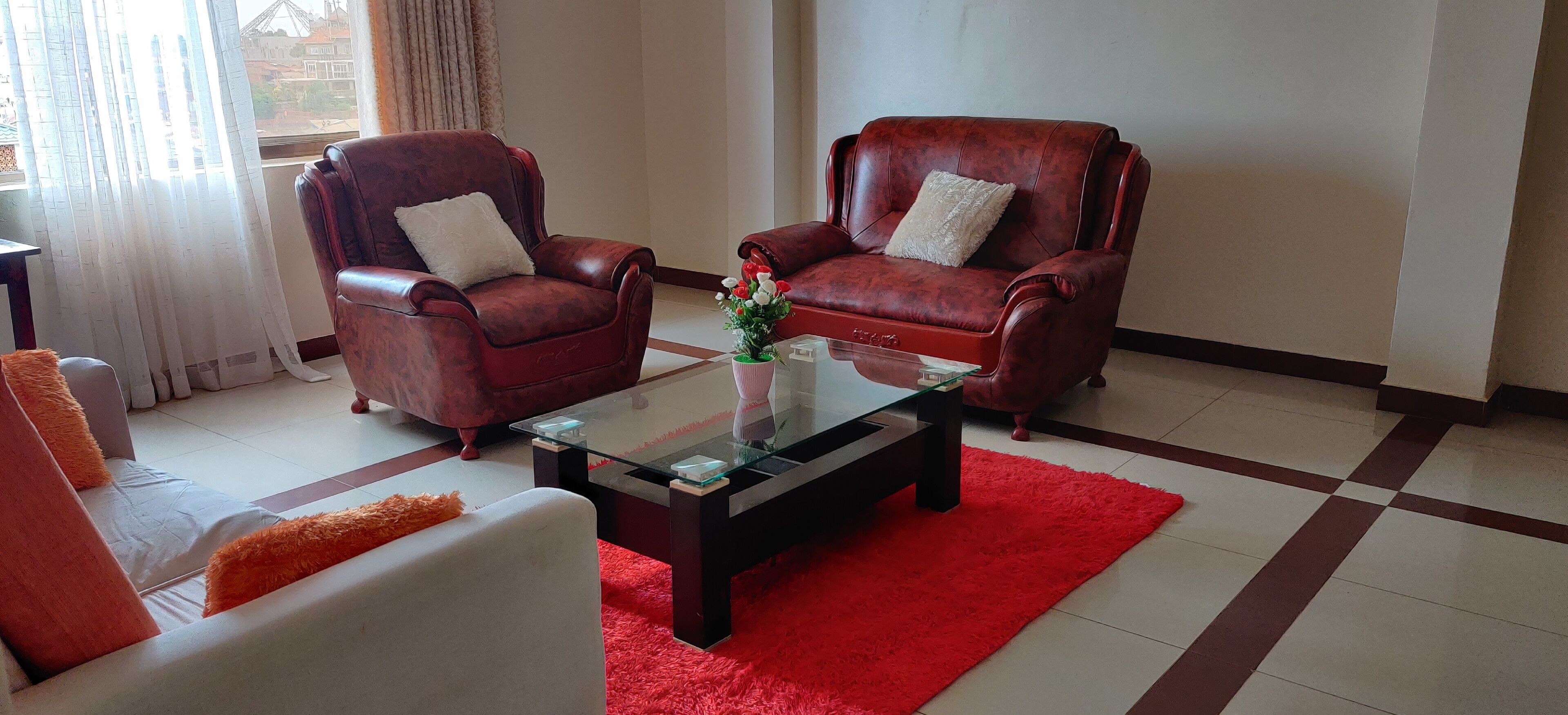 Un salon avec deux fauteuils en cuir, une table basse en verre et un tapis rouge.