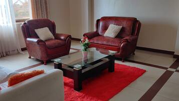 Un salon avec deux fauteuils en cuir, une table basse en verre et un tapis rouge.