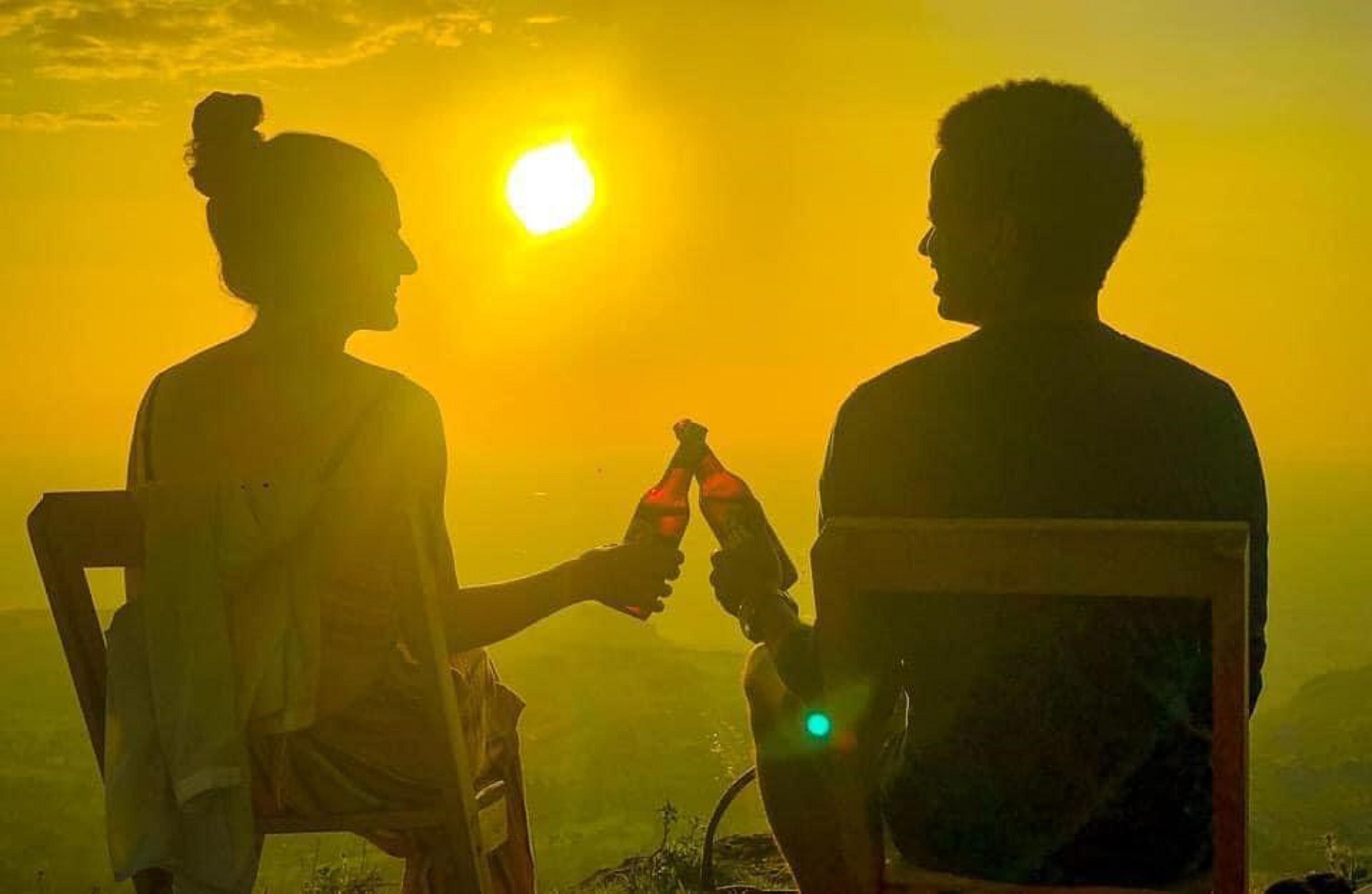 Two people sitting on chairs facing each other with a sunset in the background.