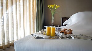 A neatly made bed with a tray of breakfast including croissants, orange juice, and a vase of yellow flowers. - Airport Hotel Entebbe (Entebbe)