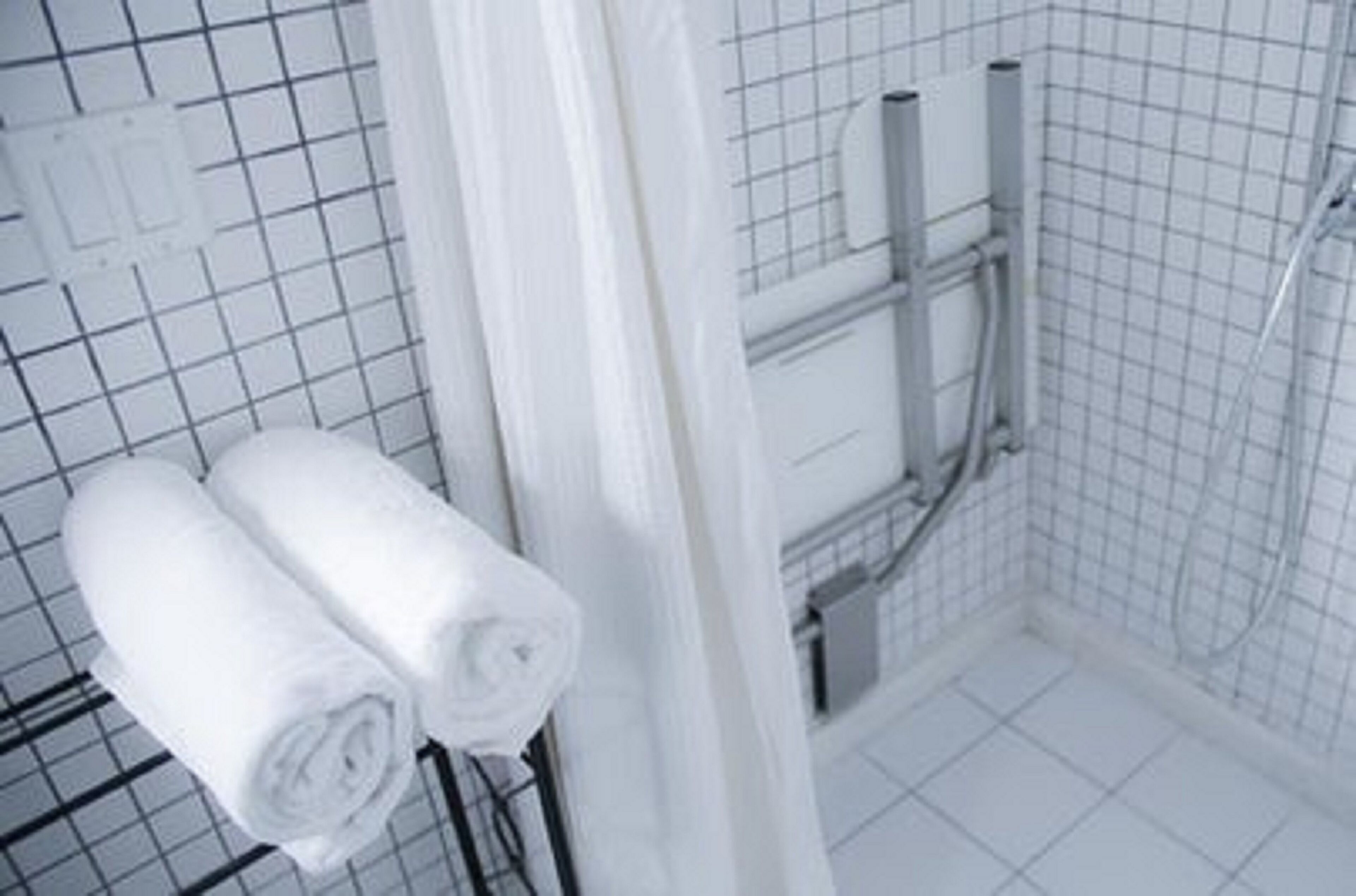 A bathroom with white tiled walls, a shower area, and two rolled towels on a rack.