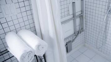 A bathroom with white tiled walls, a shower area, and two rolled towels on a rack.