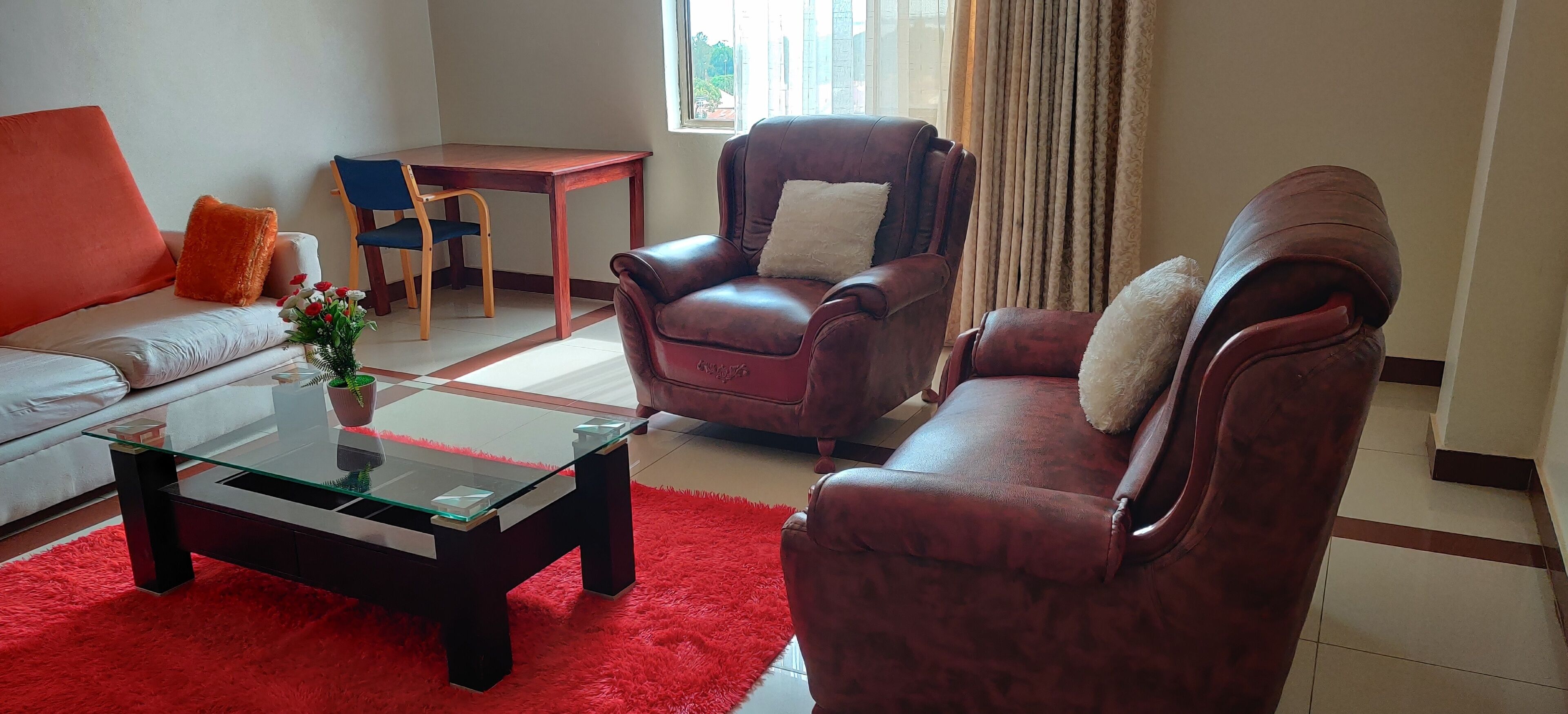 A living room with a sofa, two leather armchairs, a glass coffee table, and a small table with chairs.