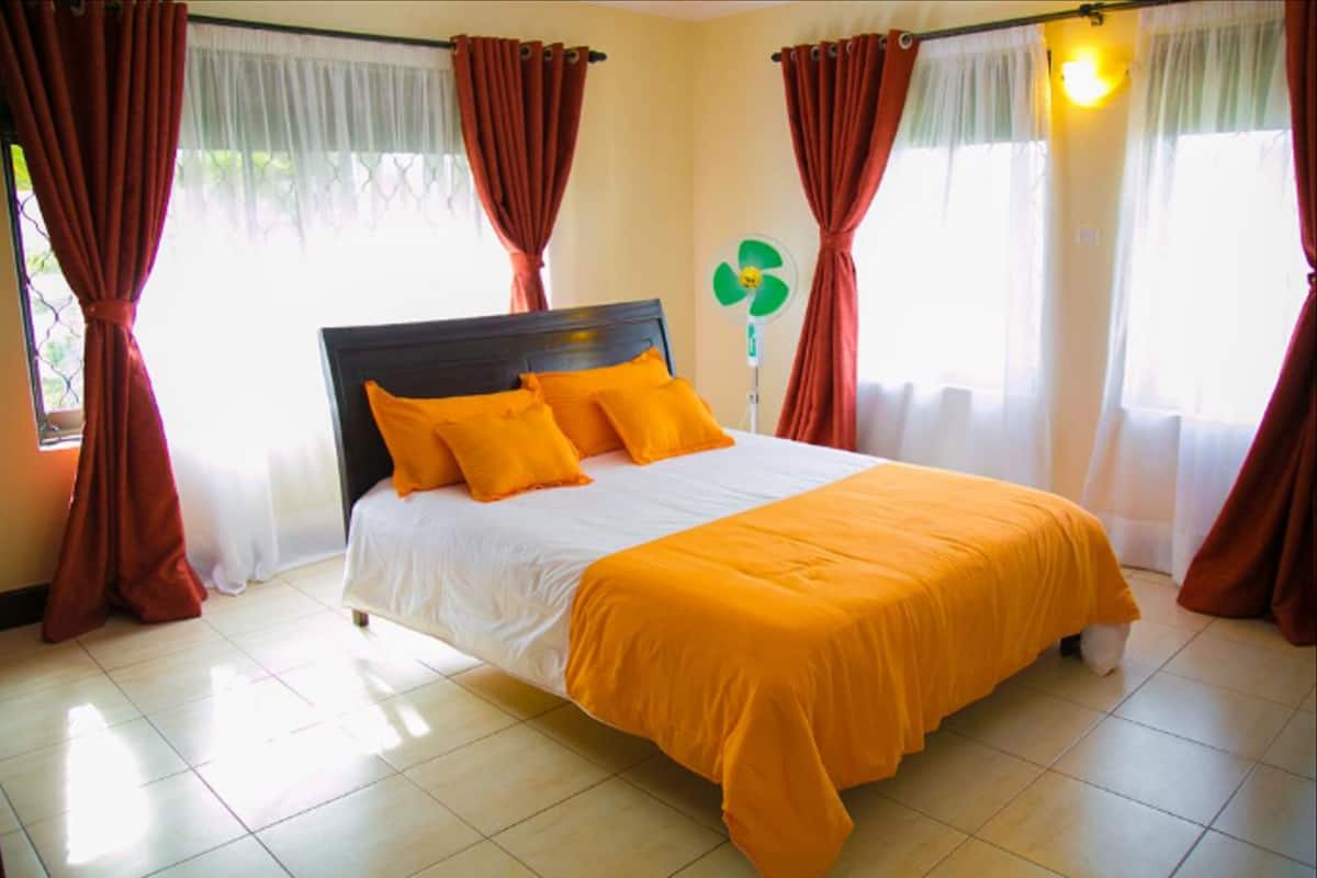 A hotel room with a bed, orange bedding, and red curtains.