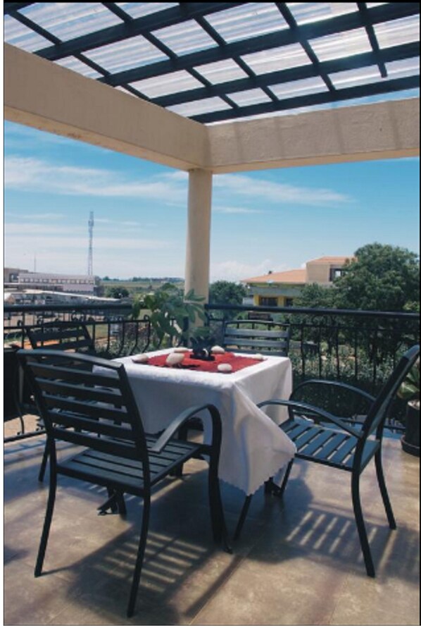 An outdoor patio with a table and chairs, a view of the cityscape, and a clear sky.