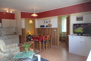 A compact kitchen with white cabinets, a dining table with chairs, a TV, and a small dining area with a table and chairs. - Apartment 15 - Baltic Sea shell (Zinnowitz)