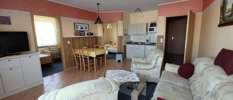 A living room with a sofa, a TV, a dining table, and a kitchen area.