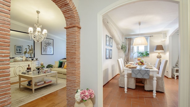 A dining area with a brick column, a chandelier, and a table set for a meal. - Spacious Home with Elevator along Via Guinigi inside the Lucca Walls (Lucca)