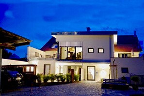 A two-story building with a balcony, a car parked in front, and a cobblestone driveway. - Apartment 3 - Guesthouse Andrea Herzig (Breisach am Rhein)