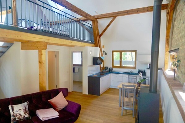 A spacious loft-style living area with a wooden ceiling, a kitchen with a central island, and a balcony with a metal railing. - Apartment 3 - Guesthouse Andrea Herzig (Breisach am Rhein)