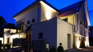 Ein modernes, zweistöckiges Haus mit flachem Dach und einem Balkon im oberen Stockwerk.