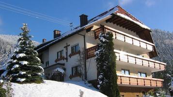 Ein mehrstöckiges Gebäude mit Balkonen, umgeben von schneebedeckten Bäumen und blauem Himmel.
