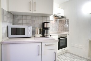 Una cocina con armarios blancos, microondas, cafetera y horno.