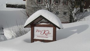 Un letrero cubierto de nieve para 'Hans Keller Ferienwohnungen', con una estructura de madera y techo nevado.