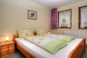 A bedroom with a wooden bed, a nightstand, a lamp, a framed picture on the wall, and a window with curtains.