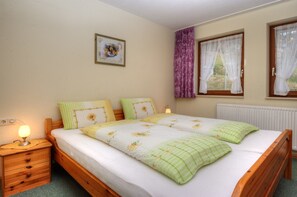 A bedroom with a wooden bed, a nightstand, a lamp, a framed picture on the wall, and a window with curtains.