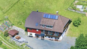 Una casa de dos pisos con techo inclinado, paneles solares y un pequeño garaje adosado.