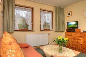 En hyggelig stue med en sofa, et bord med blomster, et fjernsyn og et træskab.